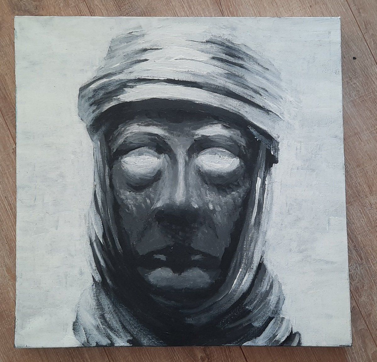A monochrome painting of a hooded face, photographed on a wooden floor